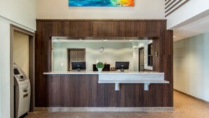 A reception desk with a wooden finish, two computer monitors, a clock, and a plant. - Clarion Inn & Suites Atlanta Downtown (Atlanta)