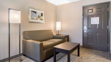 Habitación de hotel con sofá, una mesita, una lámpara, un cuadro en la pared y una puerta con un letrero.