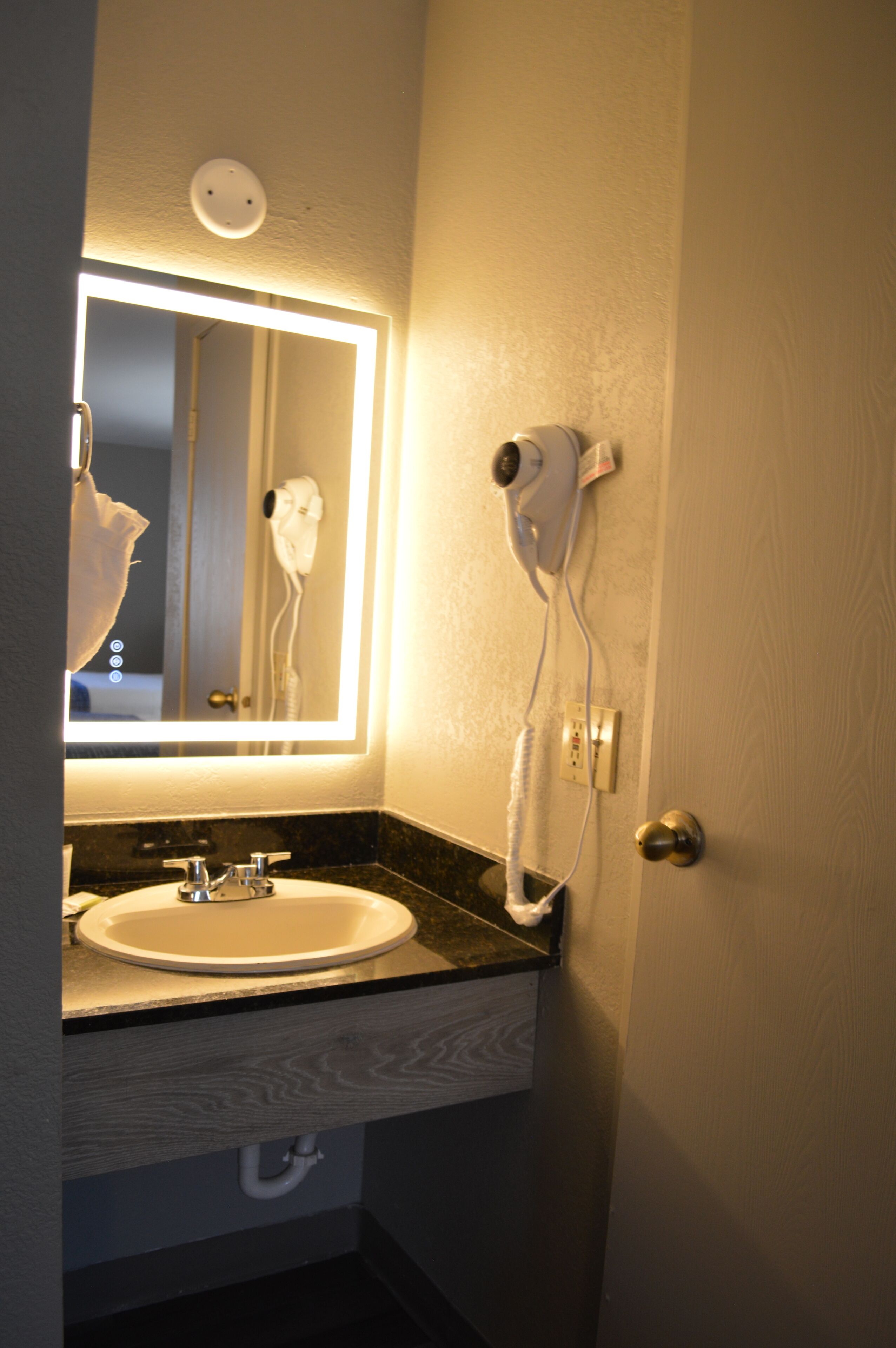 Un bagno con lavandino, specchio e asciugacapelli fissato alla parete.