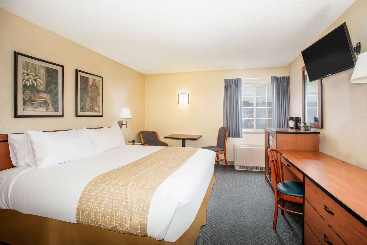 A hotel room with a large bed, a desk, a chair, a small table, a TV, and two framed pictures on the wall.