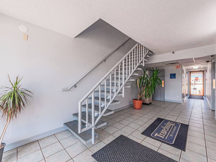 A modern hotel lobby with a staircase, potted plants, and a doormat with 'Travelodge' branding.