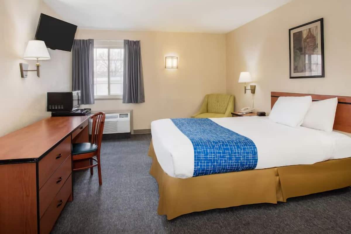 A hotel room with a bed, desk, chair, TV, and a window with curtains.