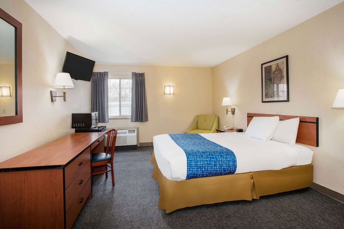 A hotel room with a bed, desk, chair, television, and artwork on the walls.