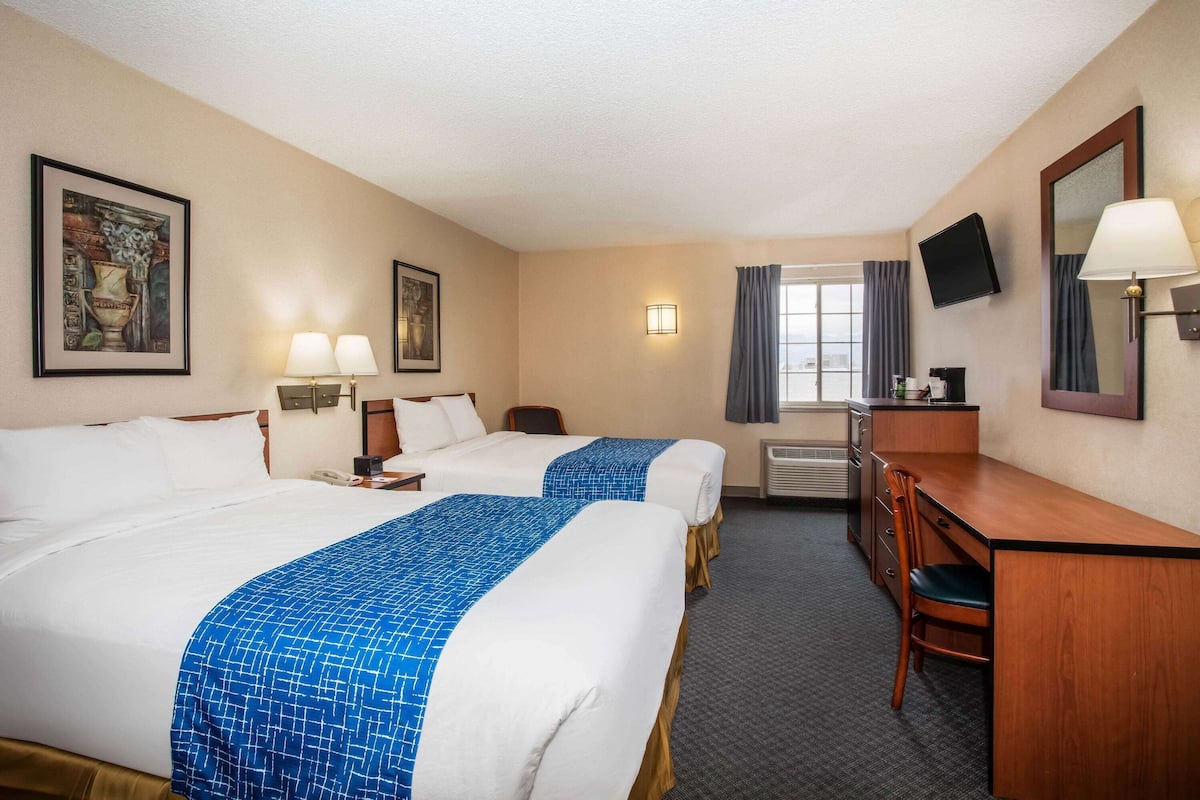 A hotel room with two beds, a desk, a chair, a TV, and a window with curtains.