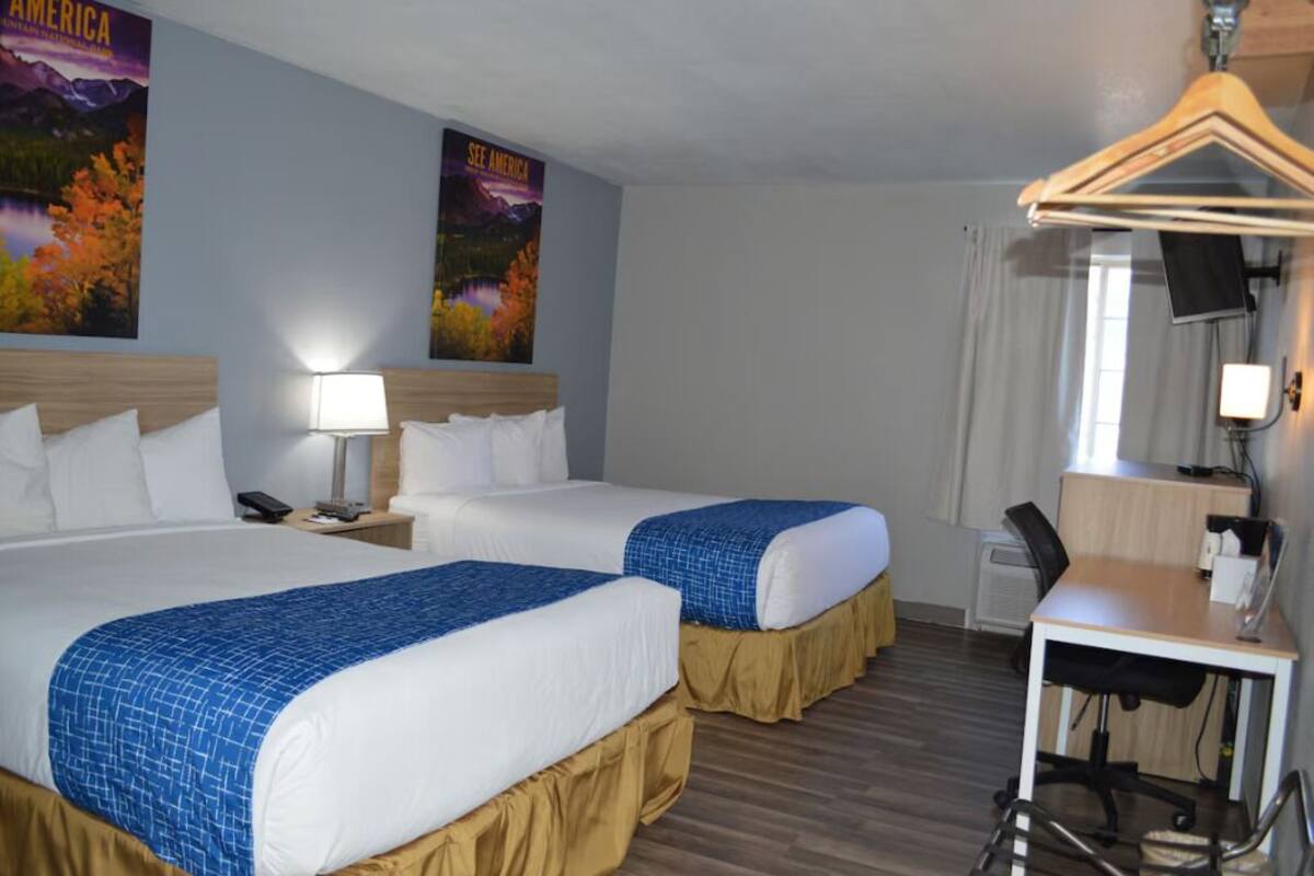 A hotel room with two beds, a desk, a chair, a TV, and a poster on the wall.