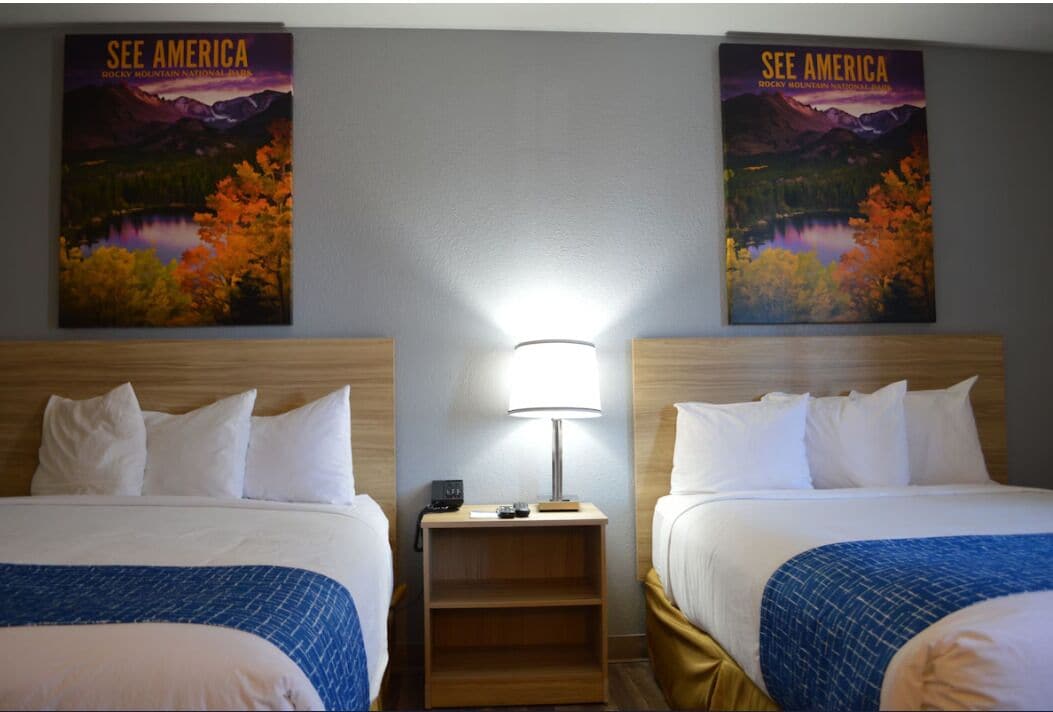 A hotel room with two beds, a nightstand with a lamp, and two posters of Rocky Mountain National Park.
