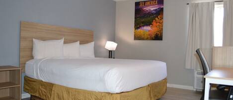 A hotel room with a large bed, a desk, a chair, a lamp, and a poster on the wall.