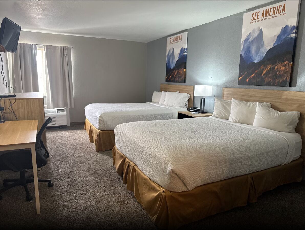 A hotel room with two beds, a desk, a chair, a lamp, and posters on the walls.