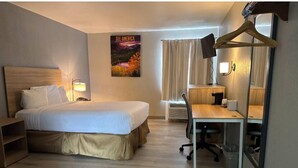 Una habitación de hotel con cama, escritorio, silla, lámpara y un cartel en la pared.