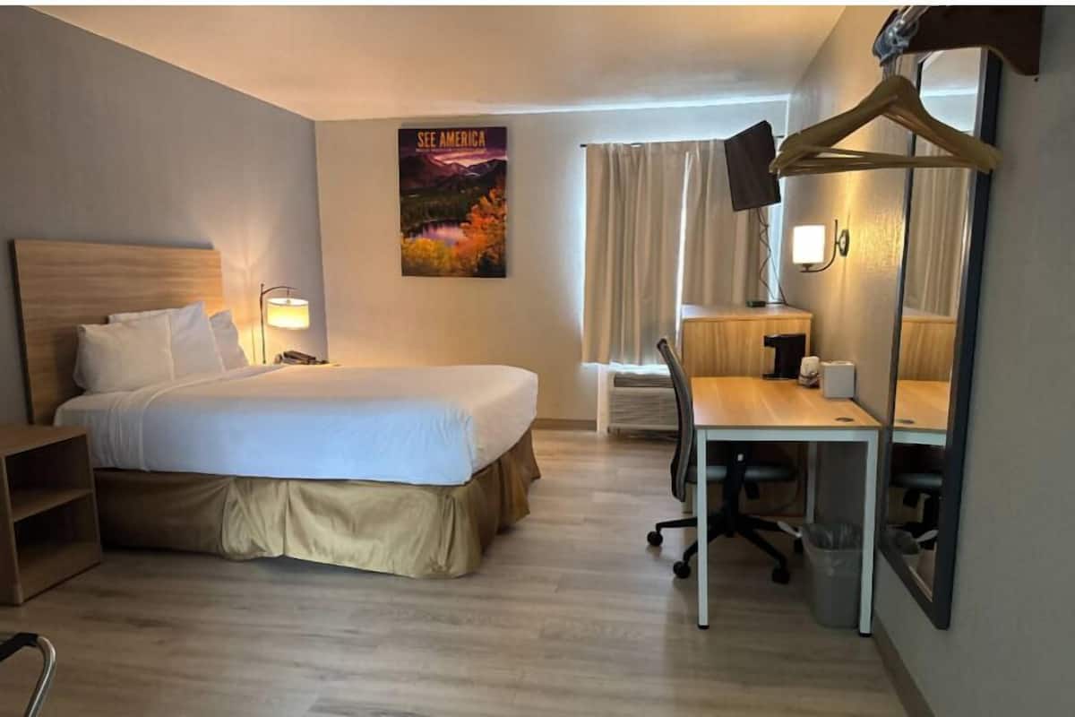 A hotel room with a bed, desk, chair, lamp, and a poster on the wall.