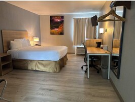 Una habitación de hotel con cama, escritorio, silla, lámpara y un cartel en la pared.
