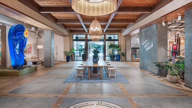 Un vestíbulo amplio con una mesa de madera central, plantas en macetas y una gran escultura azul.