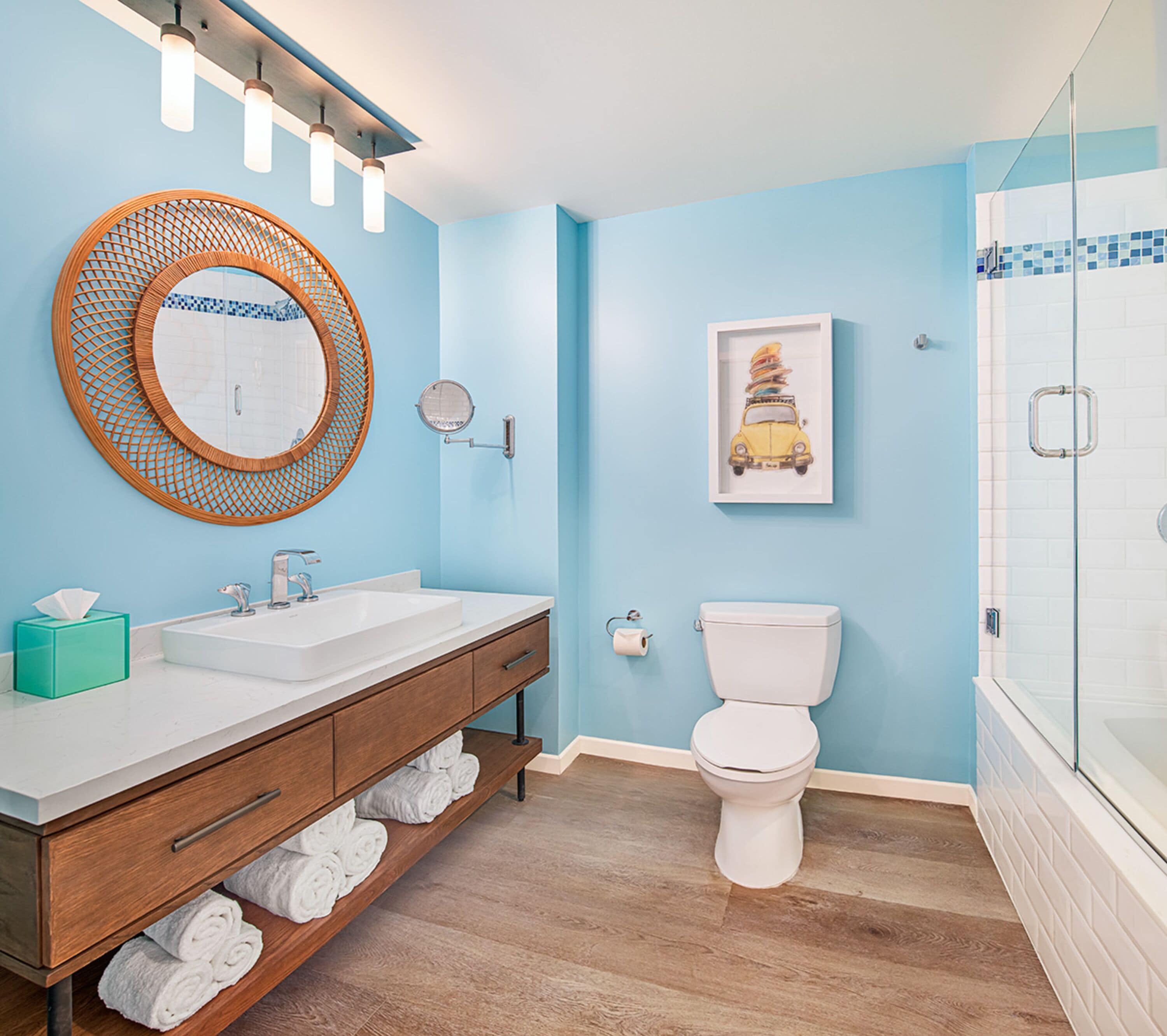 A bathroom with a wooden vanity, a round mirror, a toilet, and a framed artwork on the wall.