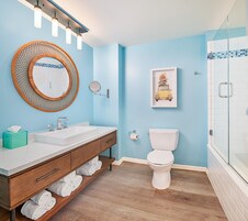 A bathroom with a wooden vanity, a round mirror, a toilet, and a framed artwork on the wall.