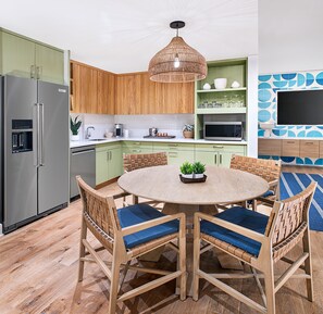 A modern kitchen with a round dining table, wooden chairs, and a hanging light fixture.