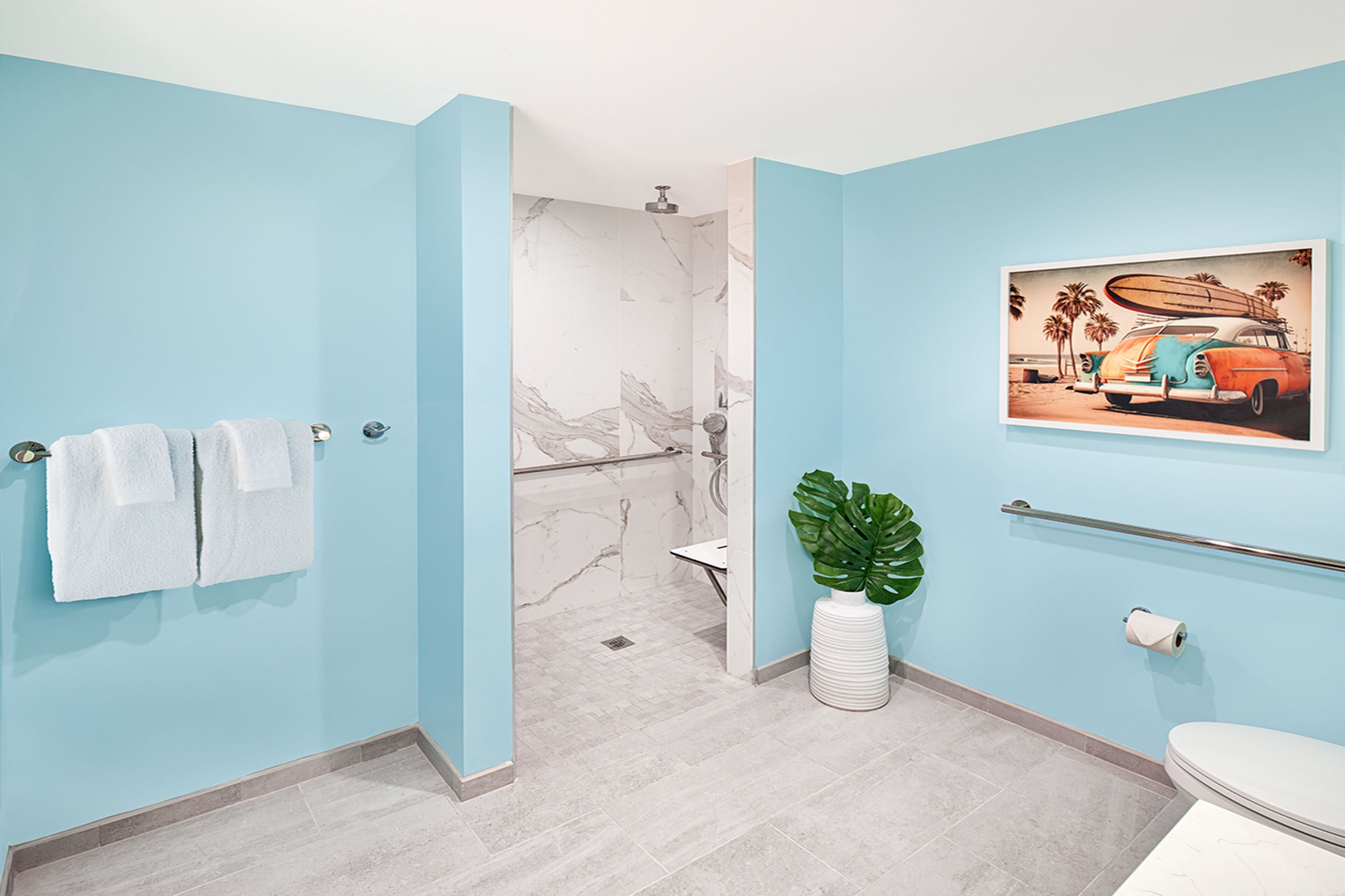 Et badeværelse med lyseblå vægge, en marmorbruser, et hvidt toilet og en plante.