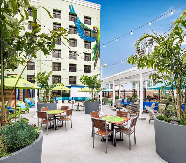 An outdoor patio area with tables and chairs, surrounded by potted plants and umbrellas. - Margaritaville Hotel San Diego Gaslamp Quarter (San Diego)