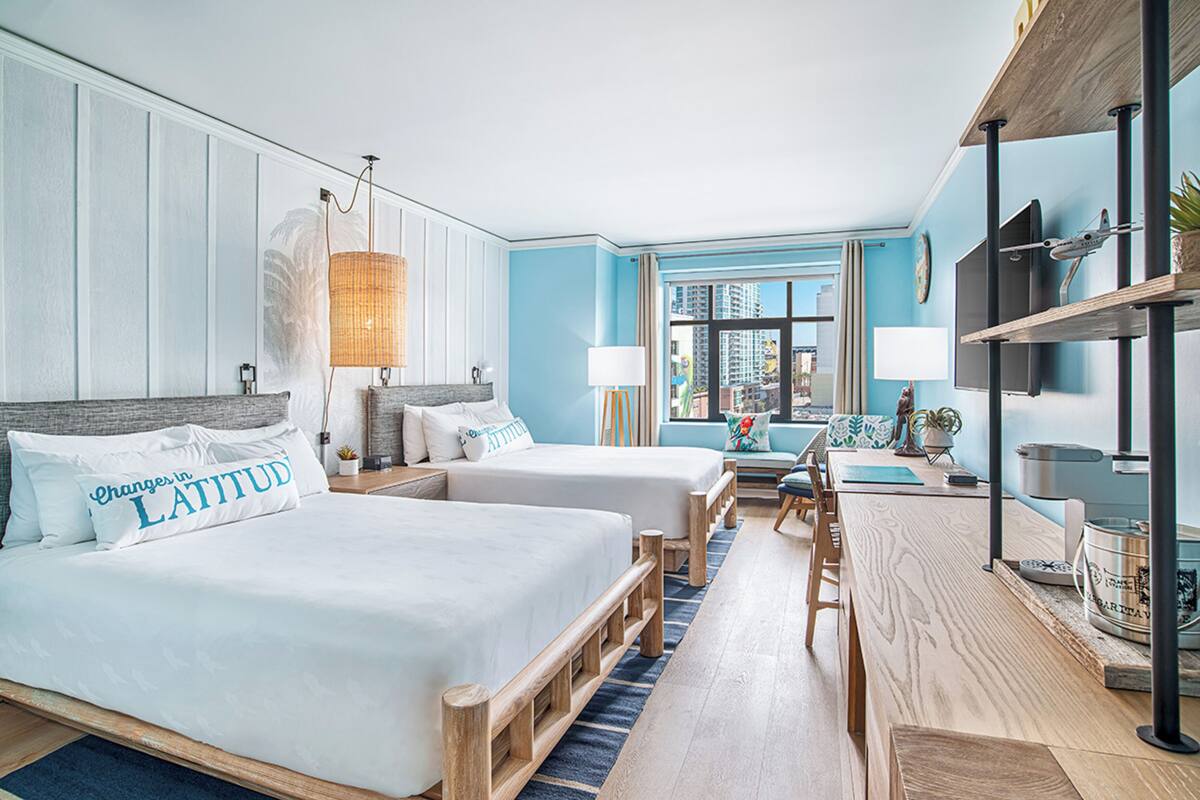 A hotel room with two beds, a desk, and a view of the city.