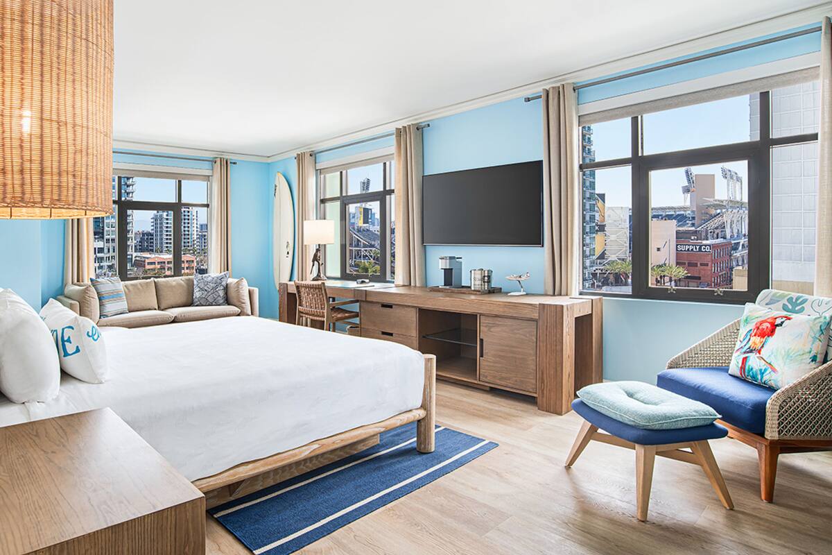 A modern hotel room with a large bed, a desk, a chair, and a TV.