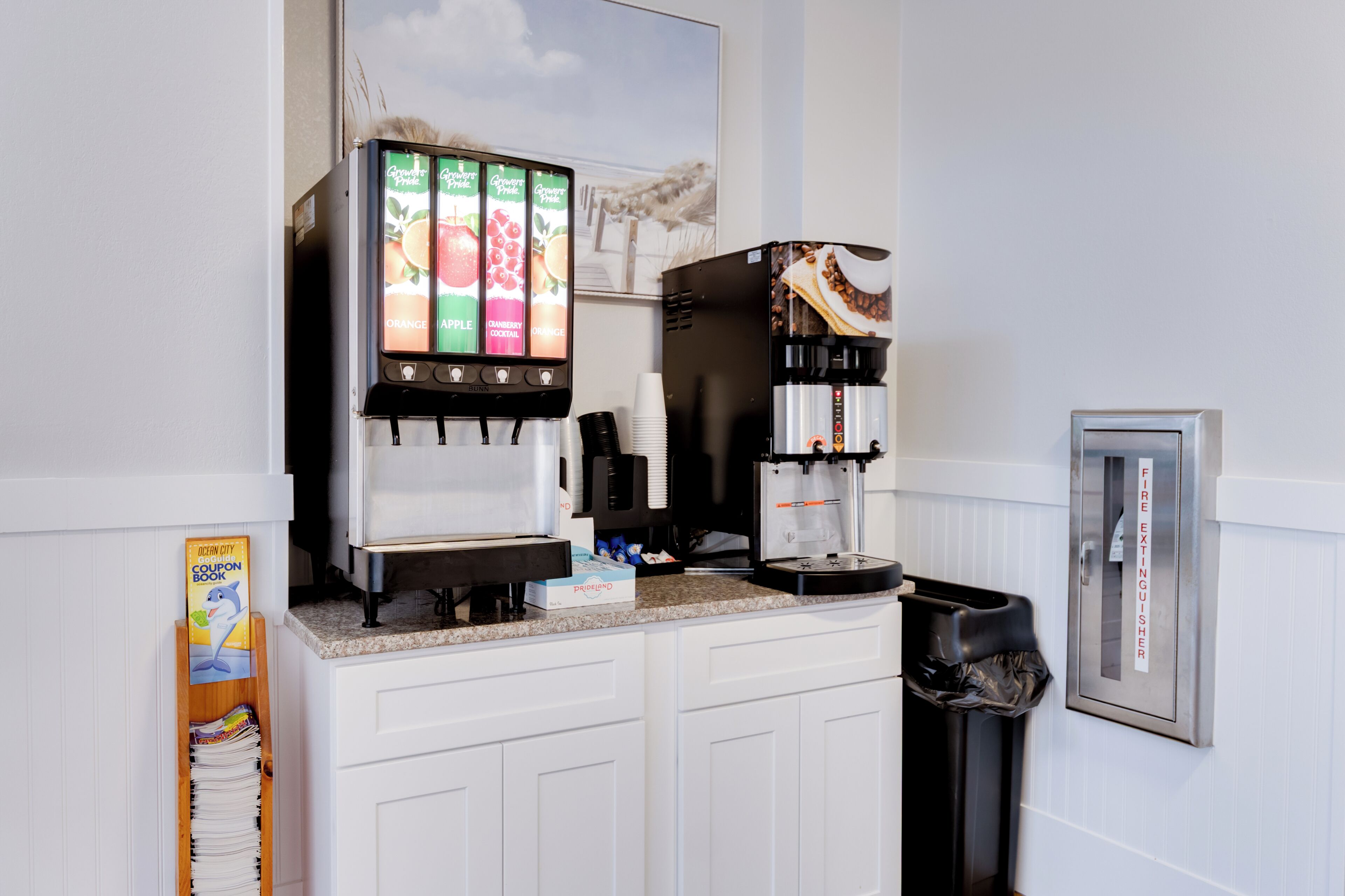 Un espace dédié au café, comprenant un distributeur de boissons, une machine à café, une poubelle et un extincteur, le tout placé sur un comptoir.