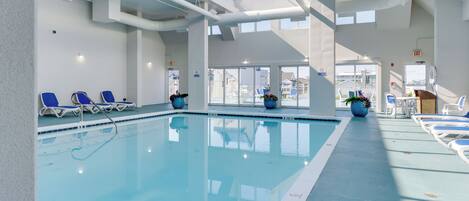 Una piscina interior con agua azul cristalina, rodeada de sillones de descanso y plantas en macetas.