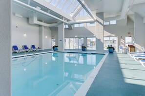 Une piscine intérieure à l’eau d’un bleu limpide, entourée de chaises longues et de plantes en pot.
