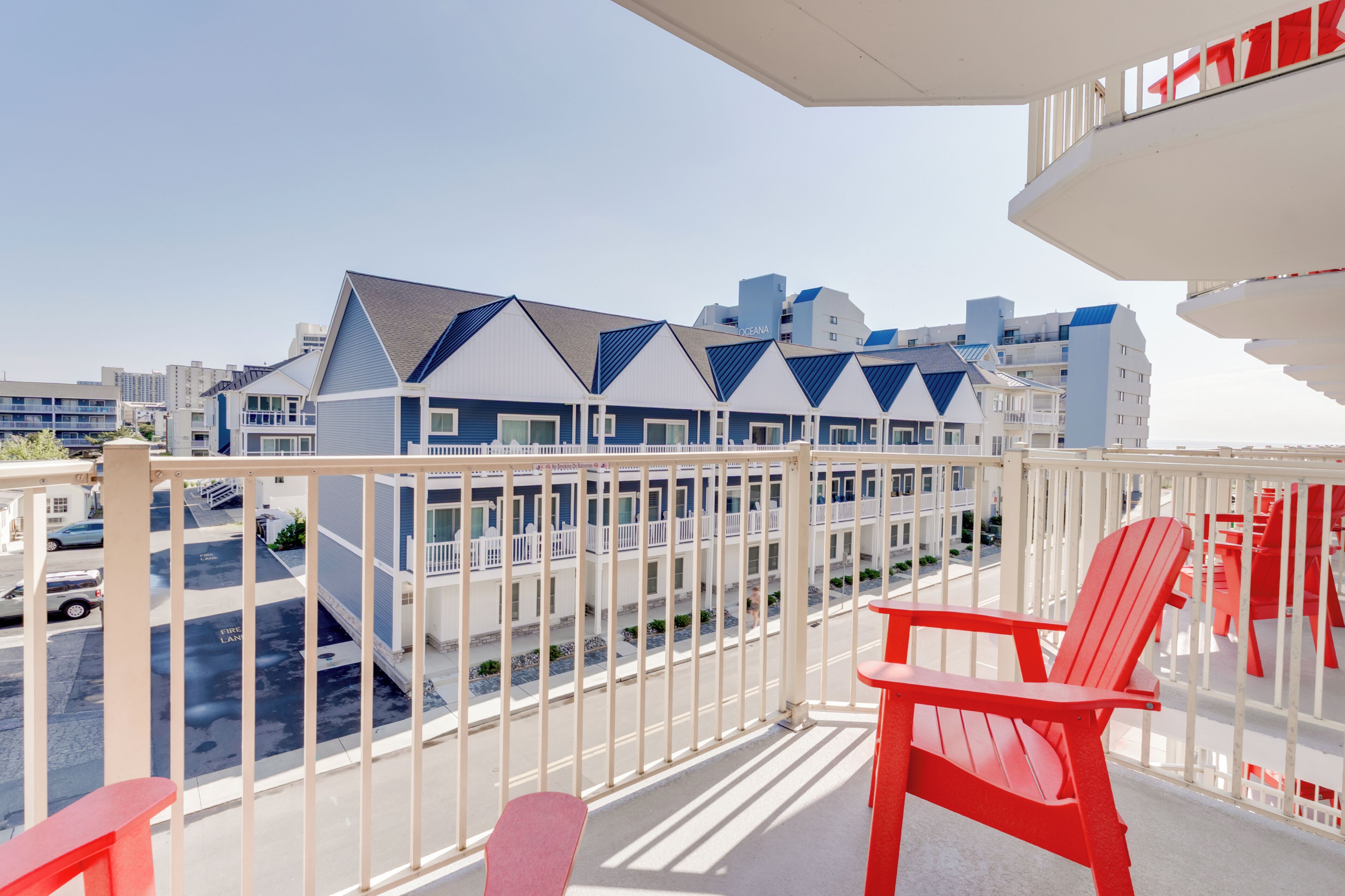 A balcony with red chairs, a view of a hotel with blue and white buildings, and a clear sky.
