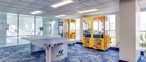A ping pong table, glass walls, and colorful claw machines in a room with a patterned carpet.