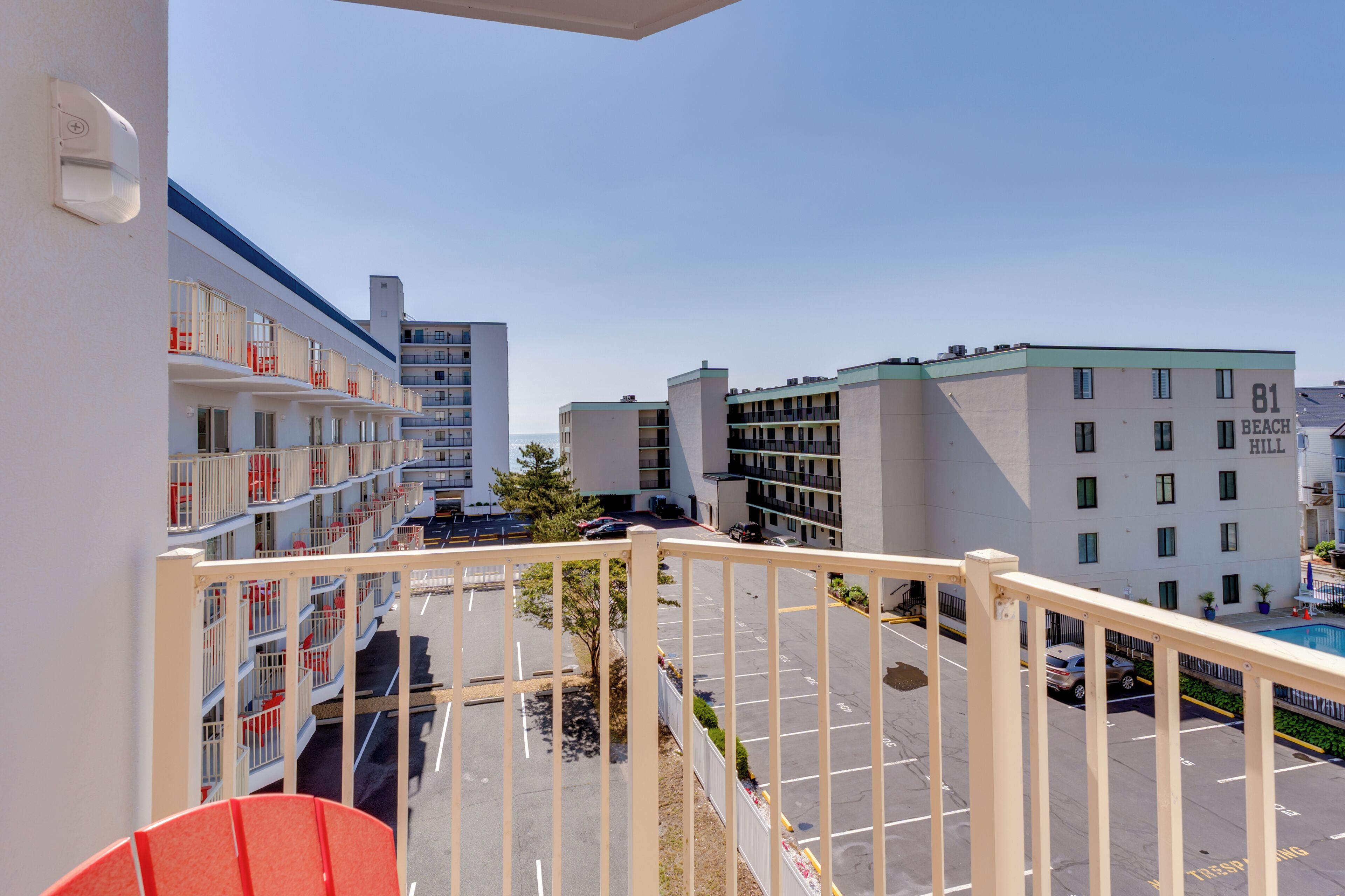 A multi-story hotel with balconies, a parking lot, and a pool area.