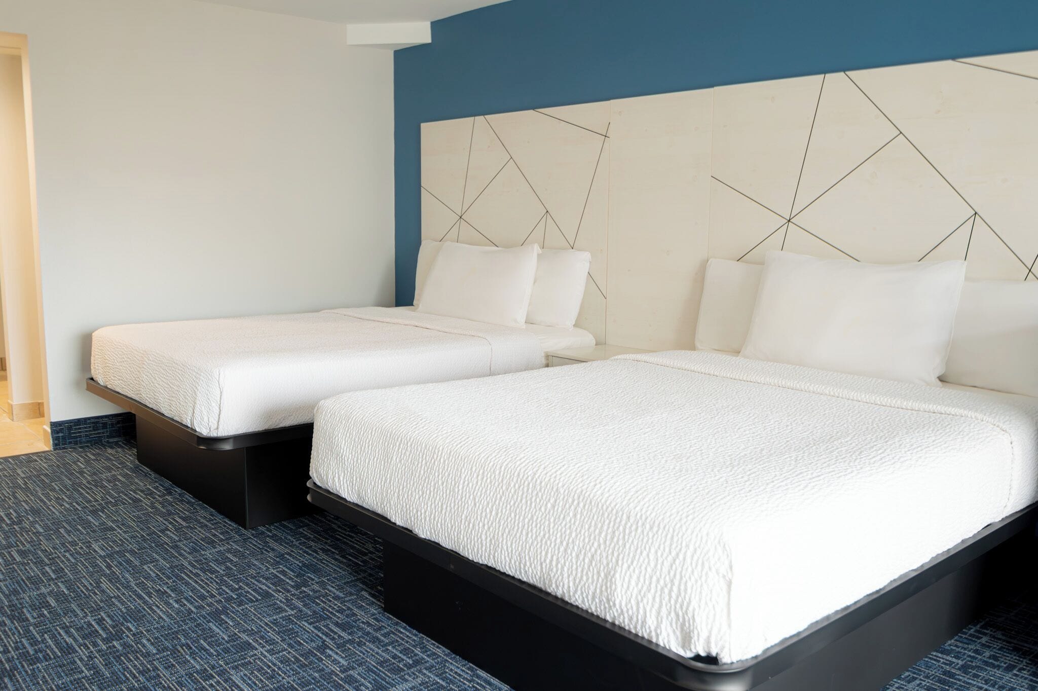 A hotel room with two beds, a modern headboard, and a blue accent wall.
