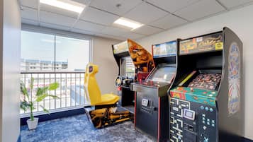 A room with arcade games, a yellow chair, a potted plant, and a view of buildings outside.