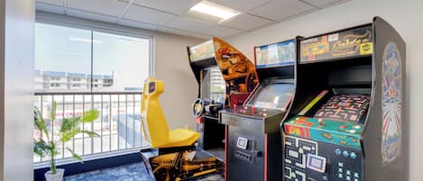 A room with arcade games, a yellow chair, a potted plant, and a view of buildings outside.