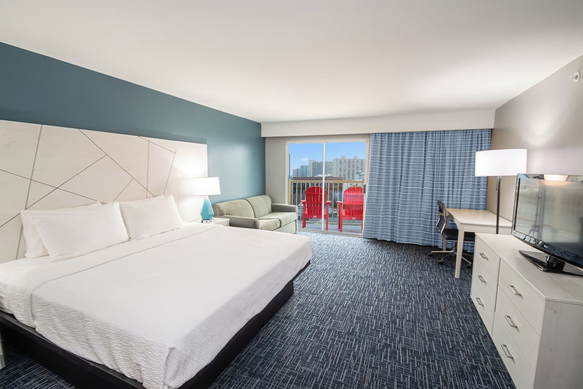 Ein Hotelzimmer mit einem großen Bett, einem Schreibtisch, einem Sessel und einem Fernseher.