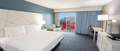A hotel room with a large bed, a desk, a chair, and a TV.