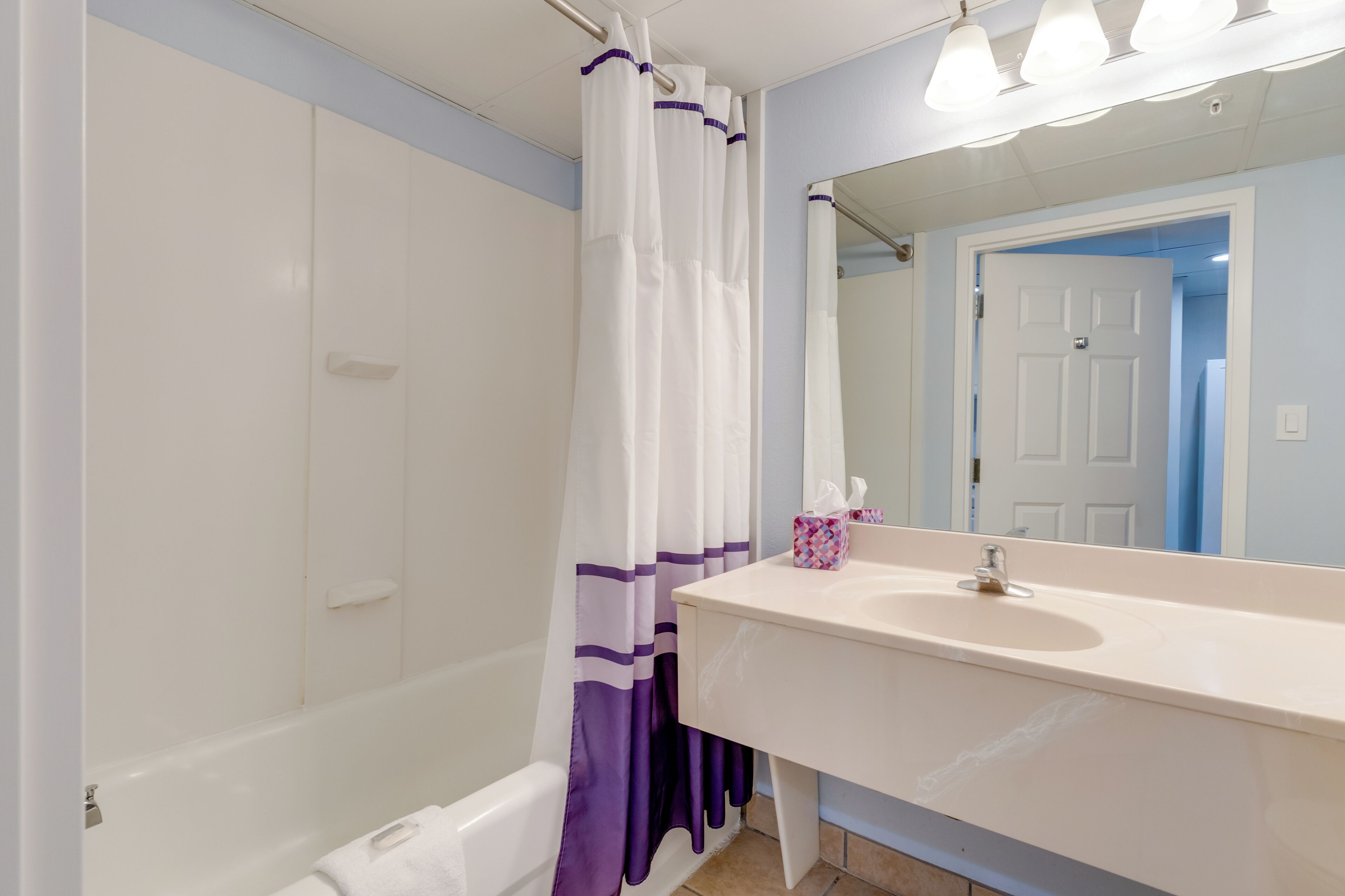 A bathroom with a bathtub, a sink with a mirror, and a shower curtain.