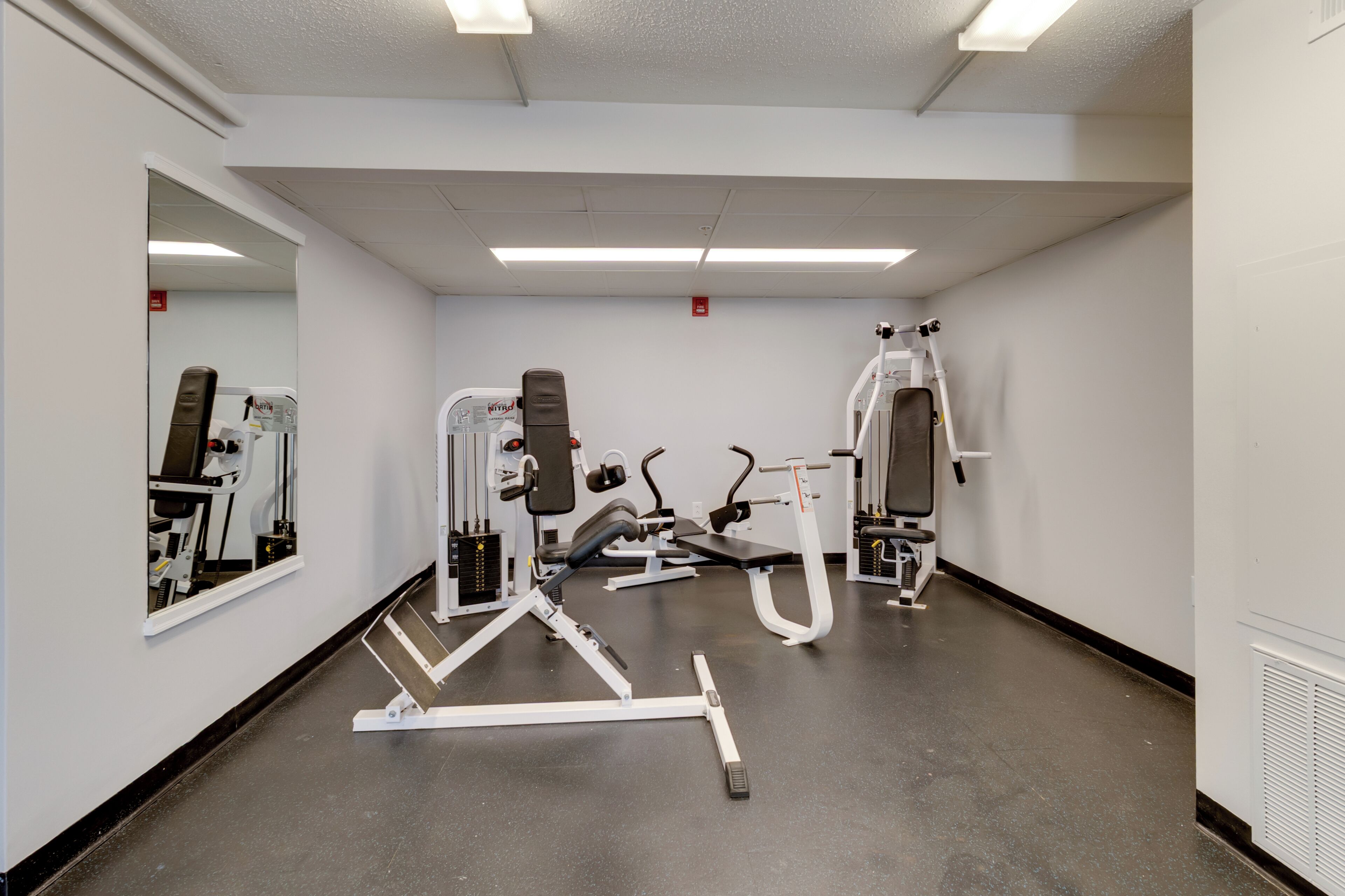 A gym with exercise equipment, a mirror, and a white wall.