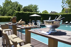 An outdoor dining area with wicker chairs, a table with a champagne bucket, and a pool in the background.