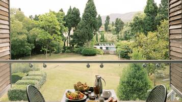 A balcony with a table set for breakfast, overlooking a well-manicured garden and a pool.