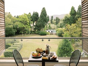 A balcony with a table set for breakfast, overlooking a well-manicured garden and a pool.