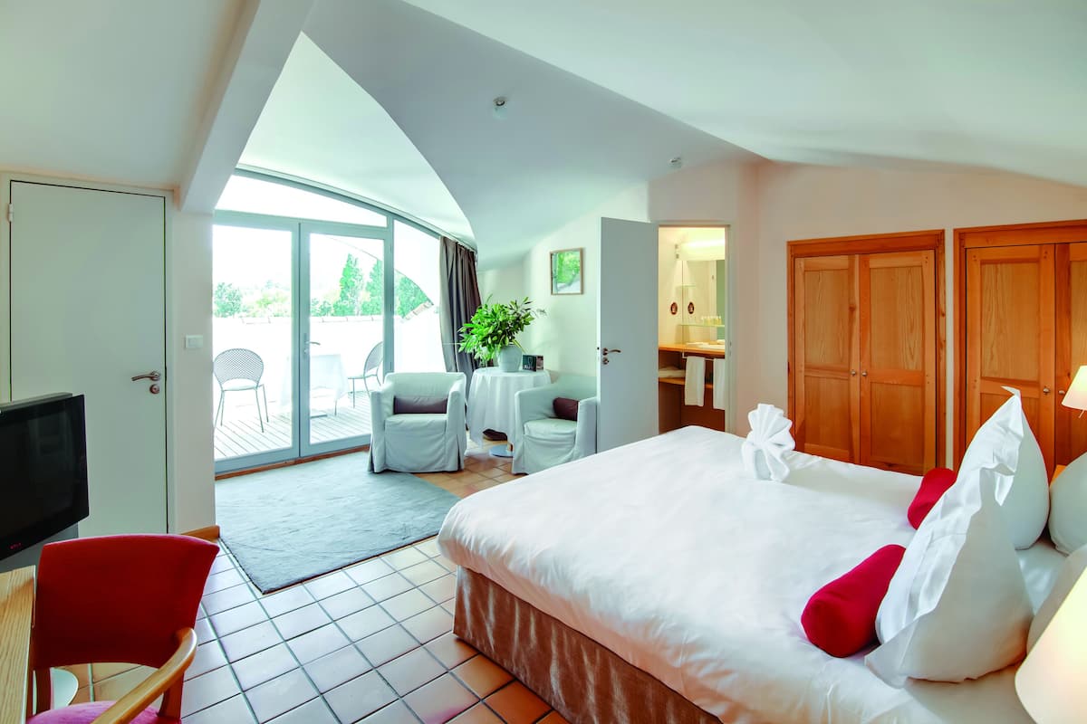 A hotel room with a bed, a TV, a desk, and a chair. There is a balcony with chairs and a table.