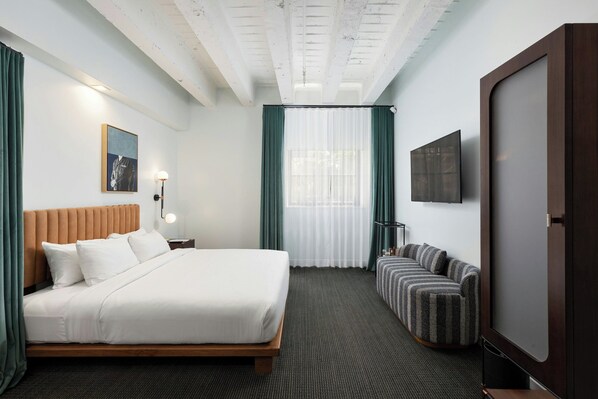 Une chambre d’hôtel avec un lit, un canapé, une télévision et une fenêtre avec des rideaux.