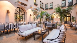 A spacious outdoor seating area with multiple tables and chairs, surrounded by large windows and potted plants. - The Guild Hotel, San Diego Downtown, a Marriott Tribute Portfolio Hotel (San Diego)