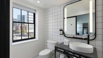 Un baño moderno con un ventanal grande, un inodoro blanco, un tocador negro con lavamanos blanco y un espejo con marco negro.