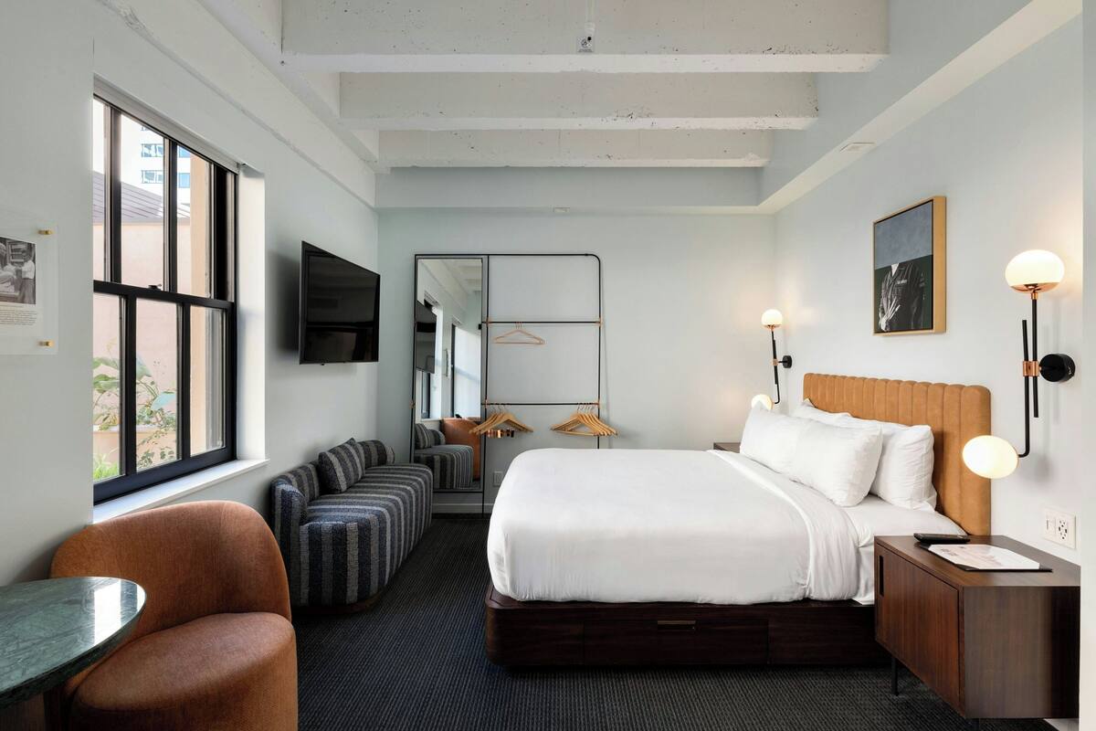 Habitación de hotel con una cama grande, un escritorio, una silla, un sofá y un televisor.