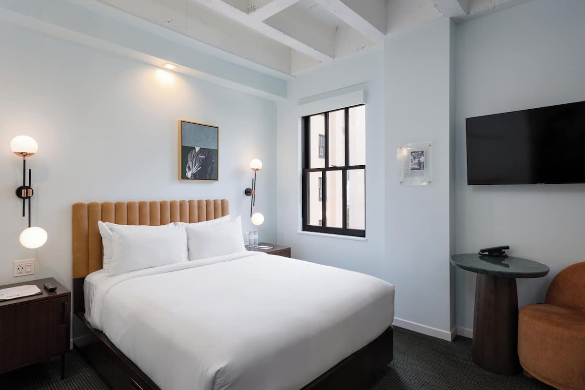 Una habitación de hotel moderna con una cama grande, un televisor, una mesita redonda y una silla.
