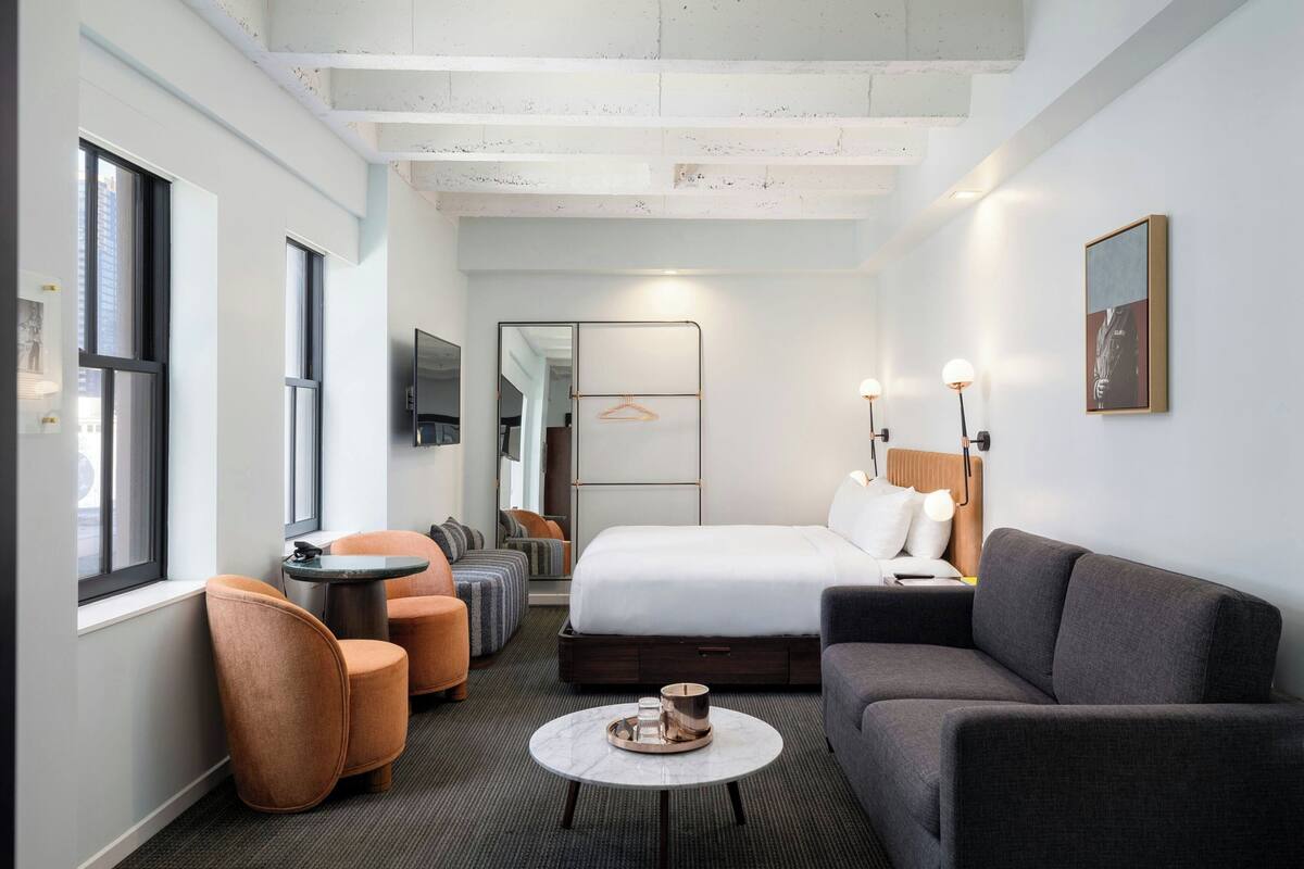 Una habitación de hotel moderna con una cama grande, un sofá, una mesita y un rincón de descanso con sillas.