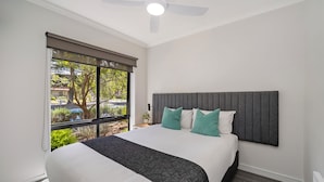Un dormitorio con cama, ventilador de techo, ventana con vistas y mesita de noche con lámpara.