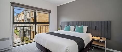 Habitación de hotel moderna con una cama grande, una mesita de noche, un ventilador de techo y vistas al exterior.