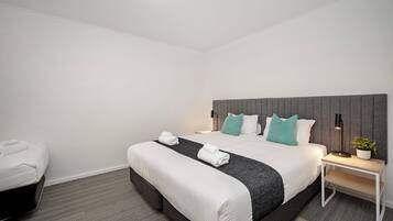 A hotel room with a bed, bedside table, lamp, and a potted plant.
