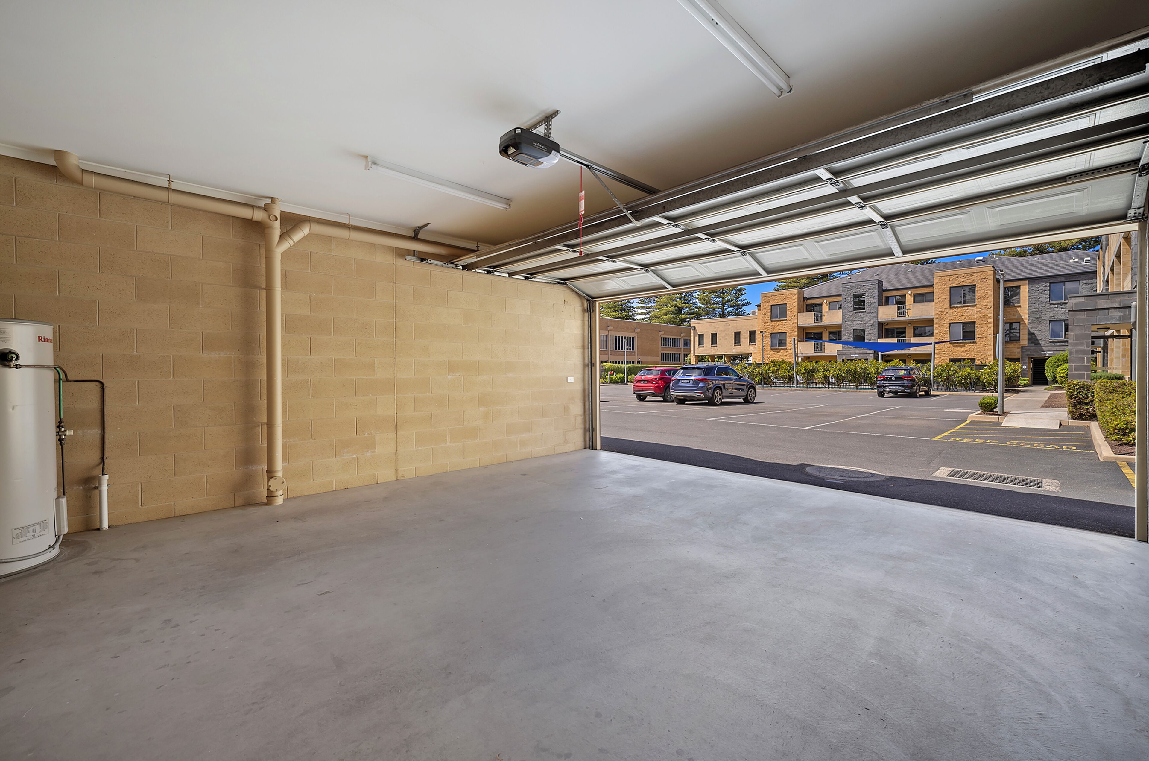 A parking garage with a clear view of the street outside, including parked cars and a building with multiple floors.